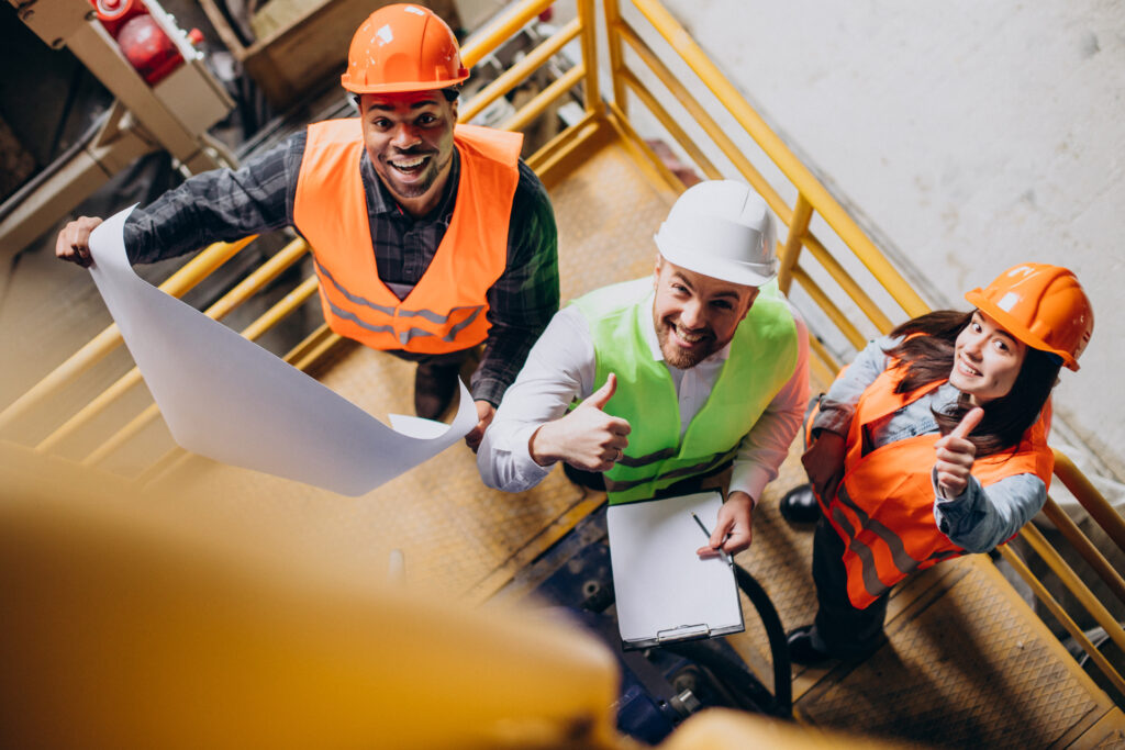 Three professionals wearing safety helmets and PPE participating in a practical industrial training session, representing skill development and workplace safety